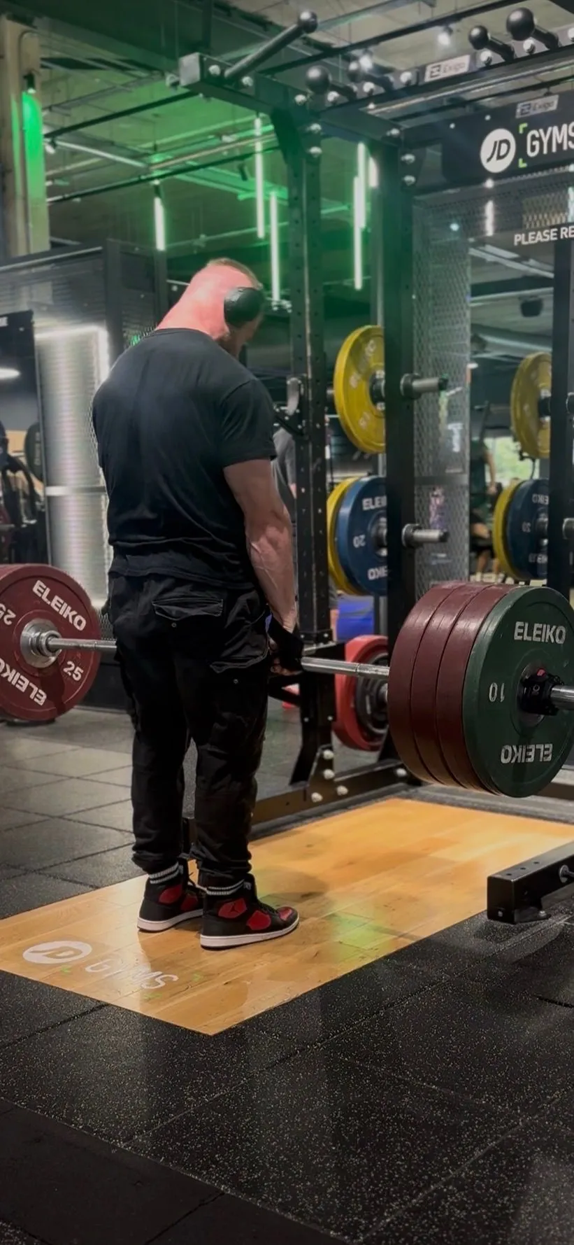 Coach deadlifting a loaded barbell in a dark gym