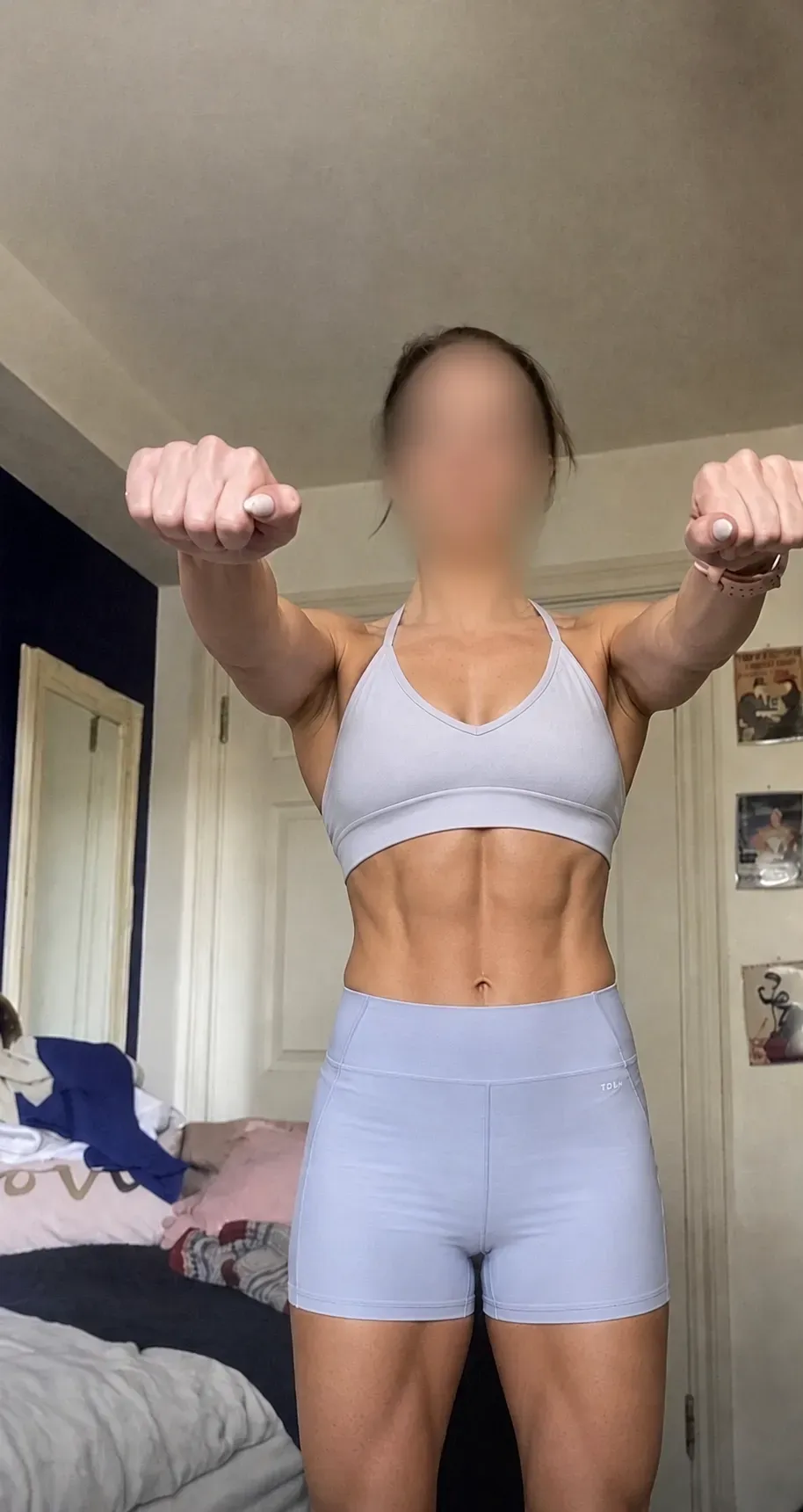 Client stands front-facing with arms raised in a light training outfit, showing a strong, defined physique